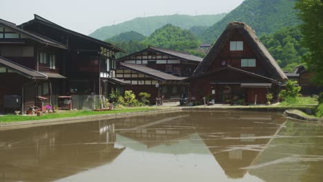 überflutetes-Feld-Vor-Traditionellen-Strohdächern,-Dorfhäusern-Und-Gebäuden-In-Shirakawago-Im-Hintergrund