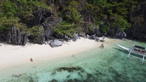 One-Island-hopping-tour-boat-at-Paradise-Beach-of-Cadlao-Island-and-tourists-snorkeling,-relaxing-on-sandy-beach-amid-tropical-scenery,-El-Nido