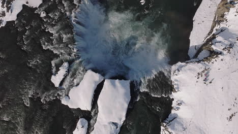 Dramatic-Top-Down-Drone-Shot-of-Goðafoss-Waterfall-on-Sunny-Winter-Day,-Glacial-Water,-Snow-and-Ice