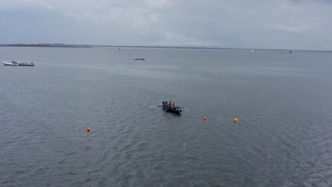 Aerial-drone-orbits-around-currach-paddle-rowing-team-as-they-approach-buoys