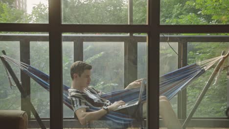 Man-Using-Laptop-While-Lying-On-A-Hammock-In-The-Balcony