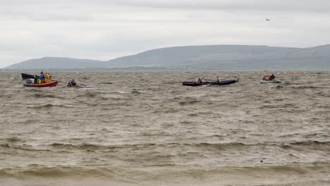 Support-crew-vessel-and-currach-boats-float-through-water,-county-clare-behind