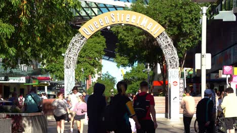 Dynamic-zoom-in-shot-capturing-Queen-street-mall-archway-sign-with-crowds-of-people,-students,-tourists-and-workers-walking-and-strolling-at-outdoor-pedestrian-shopping-mall-at-daytime,-Brisbane-city
