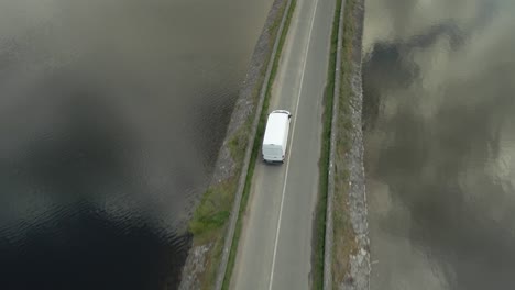Delivery-Van-Along-The-Narrow-Road-Over-Vartry-Reservoir-At-Roundwood-With-Clouds-Reflection-On-Water-In-County-Wicklow,-Ireland