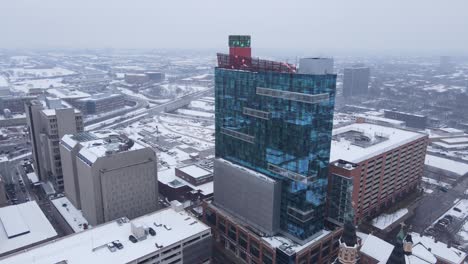 Modern-casino-building-in-downtown-Michigan-during-snowfall,-aerial-drone-view