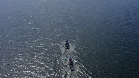 Drone-top-down-view-tracking-behind-currach-boats-rowing-in-open-ocean