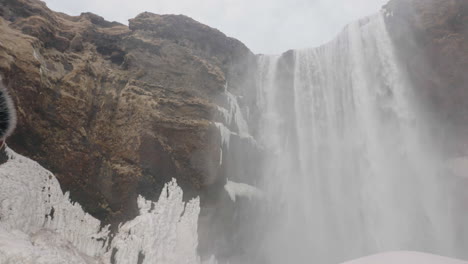 Profile-of-Middle-Age-Man-in-Warm-Clothes-and-WInter-Cap-Looking-Up-on-Waterfall-in-Cold-Landscape-of-Iceland,-Close-Up