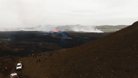 Aerial-landscape-view-of-many-people-looking-at-the-volcanic-eruption-at-Litli-Hrutur,-Iceland,-with-lava-and-smoke-coming-out