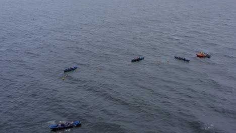 Aerial-push-in-tilt-down-above-currach-boats-lined-up-in-open-ocean-near-buoys