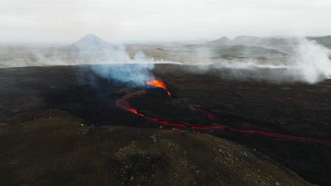 Aerial-view-of-people-looking-at-the-volcanic-eruption-at-Litli-Hrutur,-Iceland,-with-lava-and-smoke-coming-out
