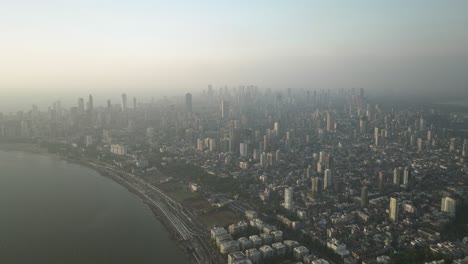 Aerial-pullback-of-Mumbai-sprawling-skyline-from-Marine-Drive-on-foggy-morning,-India