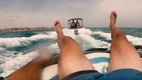 POV-water-skiing-over-inflatable-donut-pulled-by-motorboat-group-of-friends