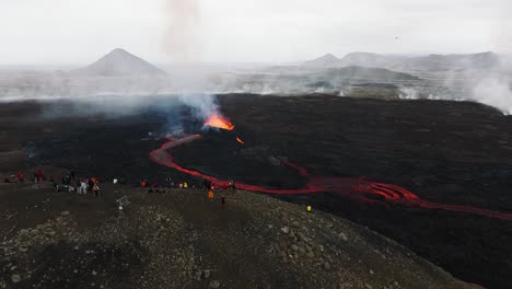 Aerial-view-of-people-looking-at-the-volcanic-eruption-at-Litli-Hrutur,-Iceland,-with-fresh-lava-and-smoke-coming-out