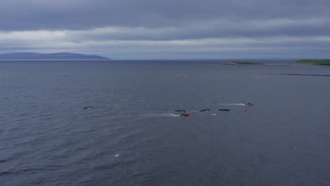 Sideview-aerial-of-currach-boat-canoes-paddling-in-open-ocean-with-support-vessel-near-by
