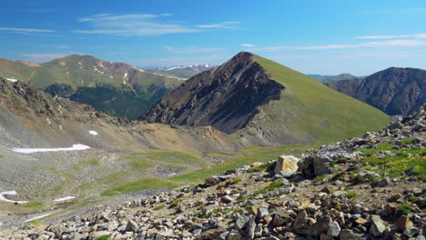 Cinematic-slow-motion-pan-to-the-left-Grizzly-Grays-and-Torreys-14er-Rocky-Mountains-peaks-Colorado-mid-day-sunny-summer-peaceful-stream-blue-sky-boulders-stunning-snow-at-top