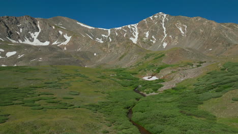 Aerial-cinematic-drone-early-morning-sunrise-hiking-trail-Grays-and-Torreys-14er-Peaks-Rocky-Mountains-Colorado-stunning-landscape-view-mid-summer-green-steam-beautiful-snow-on-top-backward-movement