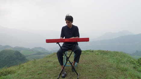 Curious-modern-asian-man-sitting-playing-piano-on-hilltop