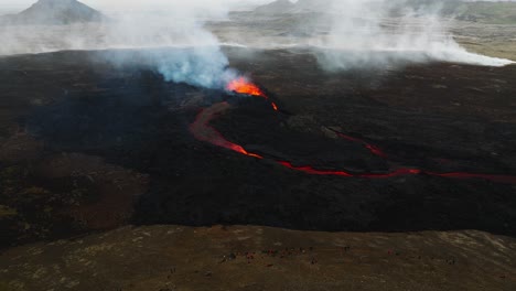 Aerial-landscape-view-of-people-looking-at-the-volcanic-eruption-at-Litli-Hrutur,-Iceland,-with-lava-and-smoke-coming-out