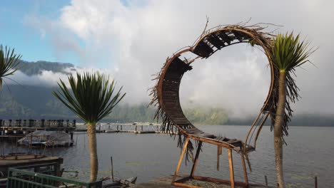 A-heart-shaped-structure-at-Beratan-Lake-in-Bali,-Indonesia-as-the-fog-in-the-distance-appears-to-be-fading-and-revealing-the-mountains-in-the-background-of-the-lake-and-boat-marina