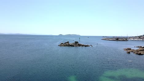 Aerial-Footage-in-Peaceful-Ocean-over-Islet-in-Marina-and-Island-in-Horizon
