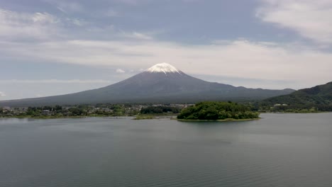 Wide-aerial-of-iconic-and-majestic-volcano-Mount-Fuji-with-scenic-landscape,-lake-Kawaguchi,-and-snow-capped-peak-in-Fuji,-Japan
