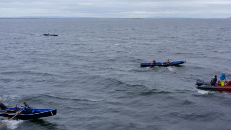 Aerial-trucking-pan-across-Currach-boats-rowing-through-ocean-by-safety-vessel