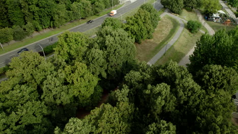 Drone-flight-over-green-trees,-revealing-a-street-with-several-traffic-lanes-and-residential-buildings
