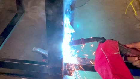 Close-up-shot-of-man-hands-wearing-red-welding-gloves-while-doing-welding-process