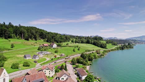 Luftaufnahmeflug-über-Ein-Kleines-Dorf-Namens-Bollingen-Am-Oberen-See-In-Der-Schweiz---Wunderschöne-Bergalpen-Und-Autos-Auf-Der-Küstenstraße-An-Einem-Sonnigen-Tag-In-Der-Natur---Schweiz,-Europa