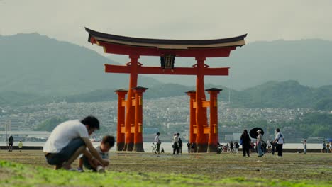 Los-Turistas-Disfrutan-De-La-Vista-Del-Gran-Giang-Torii-Rojo-Del-Templo-Del-Santuario-Itsukushima-En-Miyajima-Hiroshima,-Japón,-Antes-De-Que-Suba-La-Marea