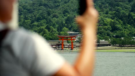 Vista-Turística-Del-Ferry-Que-Llega-A-Miyajima-Hiroshima-Japón-En-El-Fondo-El-Gran-Torii-Rojo-Gigante-Del-Templo-Itsukushima