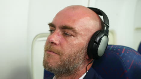 Happy-man-wearing-headphones-listening-to-music-on-a-passenger-airliner-plane-nodding-head