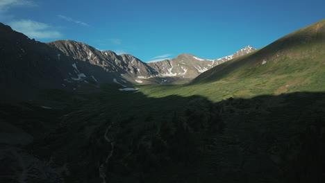 Aerial-cinematic-drone-sunrise-sunlight-early-morning-shadows-Grays-and-Torreys-14er-Peaks-trailhead-Rocky-Mountains-Colorado-stunning-landscape-view-mid-summer-snow-on-top-slowly-circle-left-movement
