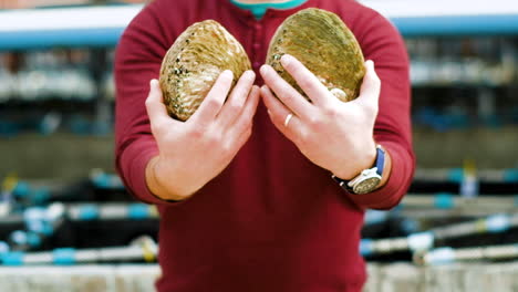 Man-holds-out-two-abalone-turns-them-so-you-can-see-the-shells,-medium-frontal