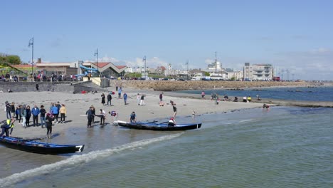 Seitliche-Schrägansicht-Von-Zuschauern,-Die-Mit-Currach-Booten-Vom-Ladies-Beach-Aus-Ins-Meer-Einfahren