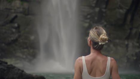 Woman-in-bikini-looking-at-splashing-waterfall-with-rock-background,-Costa-Rica