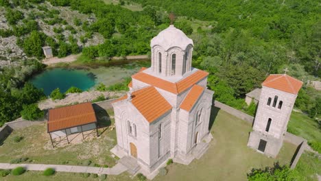 Aerial-view-of-the-sunlit-exterior-of-Orthodox-Church-of-the-Ascension-of-the-Lord-at-the-spring-of-the-Cetina-River,-Cetina,-Croatia