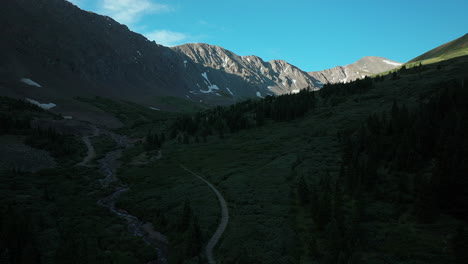 Aerial-cinematic-drone-sunrise-sunlight-early-morning-shadows-Grays-and-Torreys-14er-Peaks-trailhead-Rocky-Mountains-Colorado-stunning-landscape-view-mid-summer-snow-on-top-slowly-forward-up-movement
