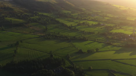 Aerial-view-tilting-over-fields-in-the-Peak-District-National-Park,-sunset-in-England