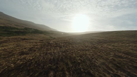 Drone-flying-towards-the-sunset-above-a-brown-hill-in-Ireland