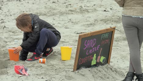Young-child-plays-and-builds-sand-castle-on-windy-day-for-competition-at-community-event