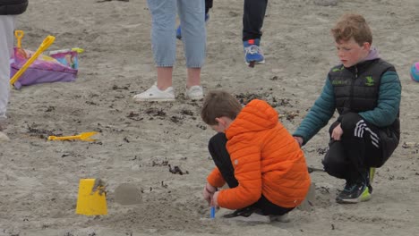 Young-boys-play-in-the-sand-wearing-puffer-jackets-at-beach