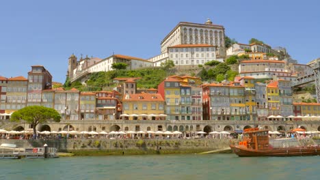 Travelling-on-the-Douro-river-by-boat,-passing-by-the-famous-Ribeira-district-of-Porto-with-lots-of-small-Port-Wine-places-beneath