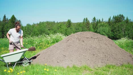 Man-At-Work-Shoveling-Soil-Into-Wheelbarrow-At-The-Farm-In-Spring