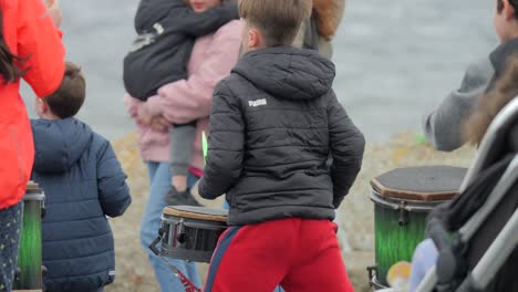 Slow-motion-close-up-of-boys-and-girls-playing-and-dancing-hitting-drums-at-beach-festival,-cold-day