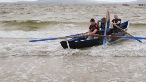 Man-sits-down-in-currach-and-quickly-paddles-oars-to-break-through-waves