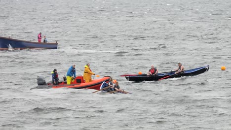 Teams-Aus-Gemischten-Männlichen-Und-Weiblichen-Ruderern-Passieren-Orangefarbene-Sicherheitsbootrennen-In-Currachs-In-Galway,-Irland