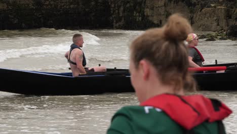Slow-motion-of-man-paddling-to-shore-in-currach-boat,-lady-in-foreground
