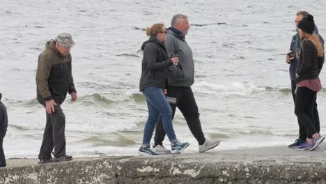 People-tourists-walk-along-sea-wall-jetty-by-beach-on-cold-day
