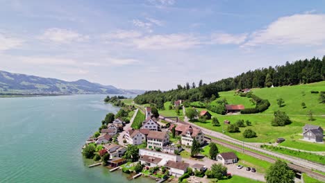 Aerial-orbit-shot-showing-idyllic-village-named-Bollingen-in-front-of-idyllic-lake-and-green-hill-scenery-in-background,-Switzerland